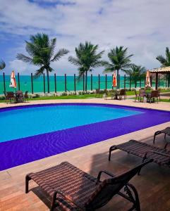a large swimming pool with chairs and palm trees at Cobertura Duplex Pé na Areia 509 Tabatinga Residence in Conde