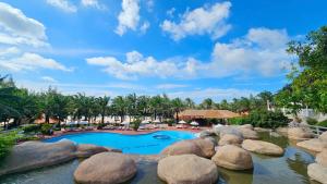a pool in a resort with rocks and palm trees at Phu Hai Beach Resort & Spa Phan Thiet in Mui Ne