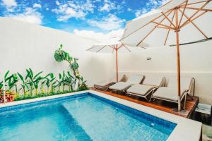 a swimming pool with chairs and umbrellas at Turtle Shelter Guest House in Sanur