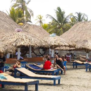 un grupo de personas sentadas en la playa bajo sombrillas en Cabañas Capilla Del Mar, en San Bernardo del Viento