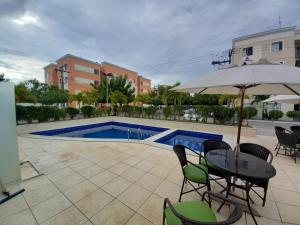 un tavolo con ombrellone e sedie accanto a una piscina di Apartamento Completo - Piscina, Pet Friendly, Academia No coração da Cidade a Feira de Santana