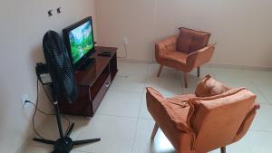 a living room with a television and two chairs at Central apartmento em Aperibé in Aperibé