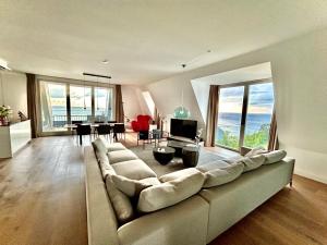 ein Wohnzimmer mit einem großen Sofa und einem Esszimmer in der Unterkunft FIRST im FIRST Sellin, Penthouse Meer & Meer mit phänomenalem Ostseeblick in Ostseebad Sellin