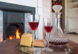 two glasses of wine and cheese on a table with a fireplace at Two Bare Feet in Waihi Beach