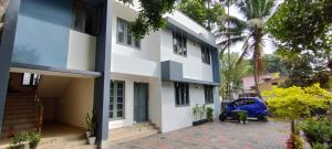a house with a blue car parked in front of it at Zora Rooms in Alleppey