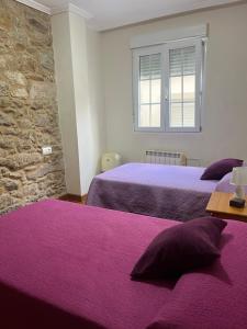 a bedroom with two beds with purple sheets and a window at La Casa de la Plaza in Cee