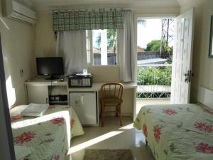 a bedroom with two beds and a television and a window at Hotel Bonnel Eirelli - Tropical in Cachoeira do Sul