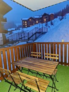 a wooden table and chairs on a deck with snow at Le studio 1800 aux pieds des pistes in Puy-Saint-Vincent