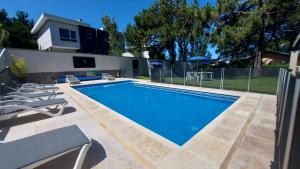 a swimming pool with chairs and a house at Picun Cuyen in Villa Gesell