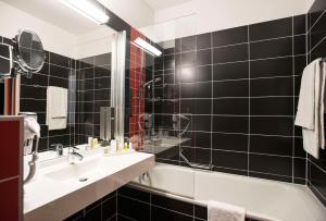 a black tiled bathroom with a sink and a tub at Best Western Plus Amedia Wien in Vienna