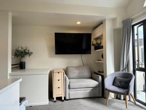 Sala de estar con silla y TV en la pared en Downtown Mt Beach Apartment, en Mount Maunganui
