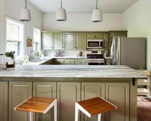 a kitchen with green cabinets and a kitchen island with two stools at Eden Brae: Historic Southern Gothic Mansion in Birmingham