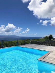 una piscina azul con terraza de madera y el océano en Villa Horizon, en Grand-Bourg