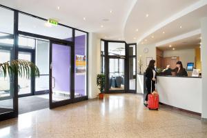 a woman with a red suitcase waiting at a counter in an airport at Best Western Macrander Hotel Dresden in Dresden