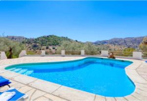 ein blauer Pool mit einem Berg im Hintergrund in der Unterkunft Cortijo Cuscurro in Ríogordo