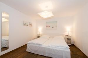 a white bedroom with a bed and a mirror at Skipperlodge - Versteck am Strom in Warnemünde