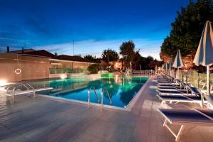 a swimming pool with chairs and umbrellas at night at Suite Apartments Prestige in Bellaria-Igea Marina