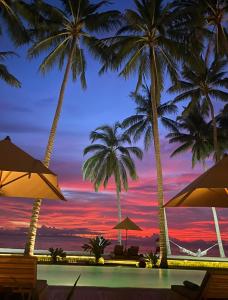 a pool with palm trees and a sunset at The Chandi Boutique Resort & Spa in Senggigi