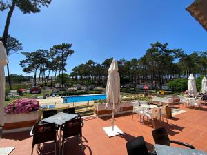 a patio with tables and umbrellas and a pool at Parque de Campismo Orbitur Valado in Nazaré