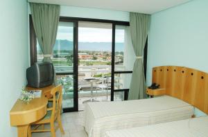 a bedroom with a bed and a desk with a television at Hotel Aojesp in Caraguatatuba