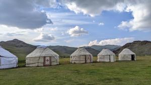 a group of four tents in a field with mountains at Yurt camp KEREMET in Kyzart
