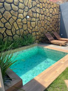 a swimming pool with two chairs and a stone wall at chalé encanto dos milagres in São Miguel dos Milagres