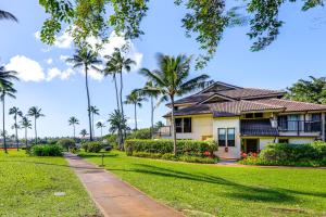 a house on a lawn with palm trees at Walk to Poipu Beaches Koloa Condo with Pool Access! in Koloa