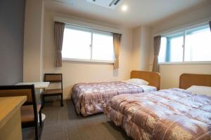ein Hotelzimmer mit 2 Betten, einem Schreibtisch und 2 Fenstern in der Unterkunft Tenpyo Ryokan in Nara