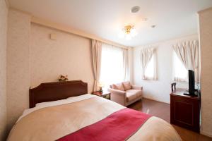 a bedroom with a bed and a chair and a television at 養老温泉ゆせんの里ホテルなでしこ in Yoro