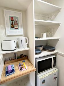 a kitchen with a microwave and a shelf with dishes at Studio Stay Narrow Neck Beach in Auckland