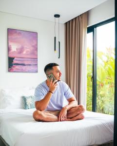 a man sitting on a bed talking on a cell phone at Wander Havens Digital Nomad Tiny Houses in Canggu