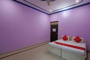 a bedroom with purple walls and a bed with red pillows at Hotel O Surprise Farm House in Alīgarh +22 photos