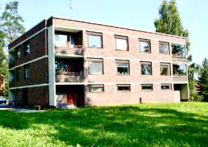a brick building with a grass field in front of it at Yksiö Jyväskylässä Savela in Jyväskylä