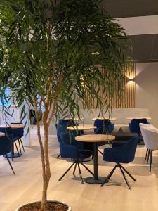 a tree in a room with blue chairs and tables at Hotel Emilia in Kaatsheuvel