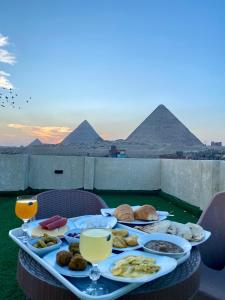 a table with food and drinks and pyramids in the background at Isis Pyramids View Inn in Cairo