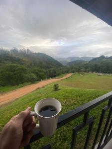 a person holding a cup of coffee on a balcony at Refúgio nascer das águas in Gravatal