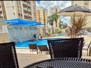 a table and chairs with an umbrella and a swimming pool at Eldorado Flat Service apto 601- BL 1 in Caldas Novas