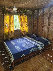 a bed in a room with yellow curtains at Mananambal Beach Huts - Family hut in Nagbalaye