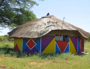 a small hut with a thatched roof in a field at Lodge Huge Dassie in Bela-Bela