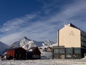 a building in the snow with mountains in the background at VISTA Gudauri - White decision in Gudauri