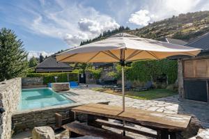 einen Holztisch mit einem Sonnenschirm neben einem Pool in der Unterkunft Kiwi Ski Cottage - Wanaka Holiday Home in Cardrona