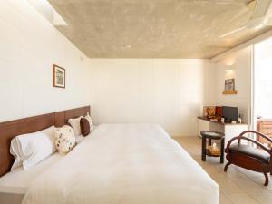 a bedroom with a large white bed and a chair at 413 Hamahiga Hotel＆Cafe in Uruma