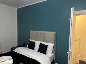 ein blaues Schlafzimmer mit einem Bett mit schwarzen und weißen Kissen in der Unterkunft Kyoto Central I 4 BDR House I 50 inch Smart TVs in Rooms I Large Spacious Rooms I Refurbished I Derby City Centre in Derby