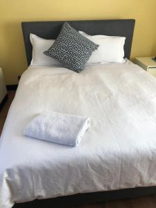 Una cama con sábanas blancas y almohadas. en Nyumbani, en Kempton Park
