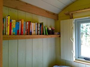 uma prateleira cheia de livros ao lado de uma janela em Chez Marguerite Luxury Shepherd's Hut em Holt