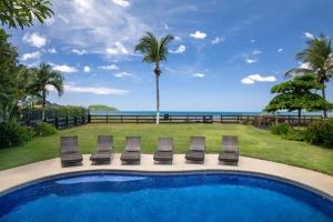 a pool with chairs and a palm tree and the ocean at Newly Renovated Beachfront Condo with Inviting Minimalist Design, Pool & Balcony with Ocean Views in Playa Flamingo