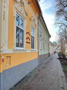 a yellow building with windows and a sidewalk at Gesztenye Apartman in Makó