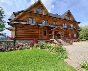 a large wooden house with flowers in front of it at Domek, Apartamenty i pokoje Willa Elita in Kościelisko
