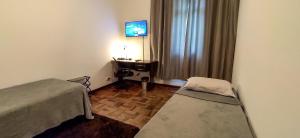库里提巴Quarto da Fê, central, perto de tudo o que você precisa!的一间有两张床和一台挂在墙上的电视的房间