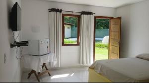 a bedroom with a bed and a television and a window at Suíte Santo in Santa Cruz Cabrália